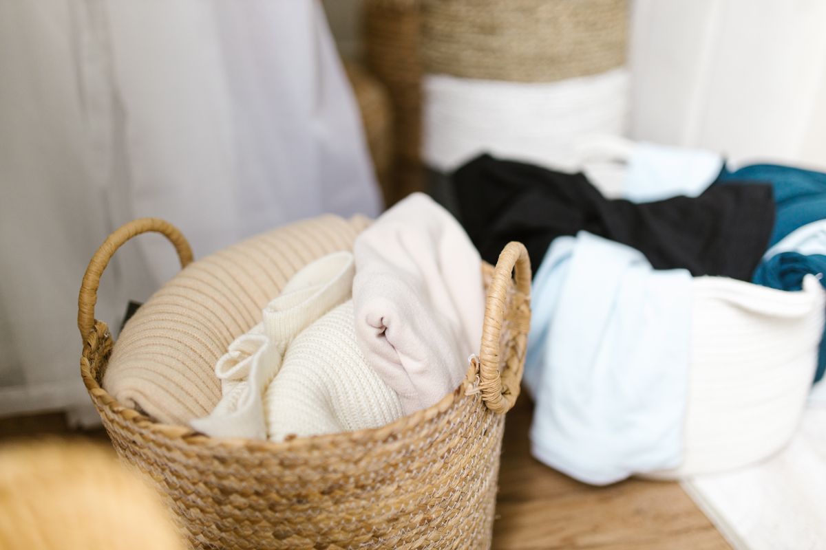 A rolling clear plastic storage bin being pulled out from underneath a wooden platform bed in a tidy bedroom, filled with folded blankets and off-season clothing