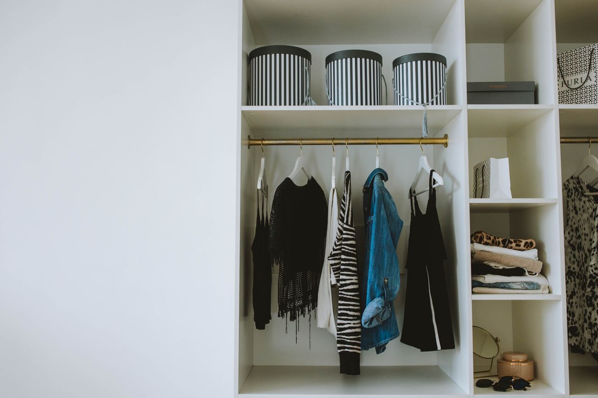 A white wooden wardrobe cabinet with neatly hung clothes visible inside, photographed in a tidy bedroom